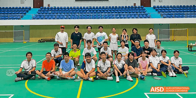 A group photo of students and faculty from the International Department of Chengdu Shude High School sitting together on a gym floor after a sports activity.