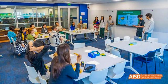 Students from the International School of Beijing collaborate on a project on a table covered in paper.