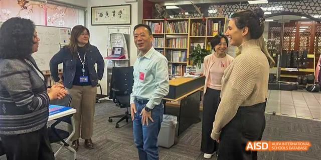 Students from the International School of Beijing are shown talking with an adult in a school hallway.