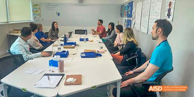 A group of students and teachers from the International School of Beijing are shown talking around a table in a meeting.