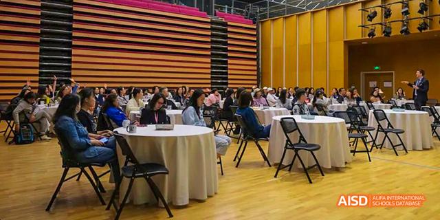 A large group of parents and teachers from the International School of Beijing are seated in an auditorium.