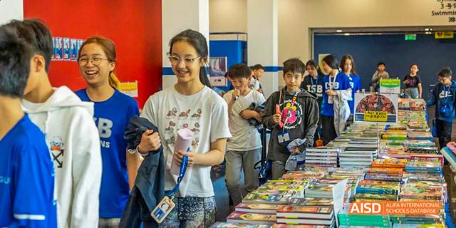 Students from the International School of Beijing are shown looking at books or items at a school fair.