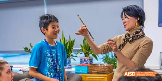 An excited young student from the International School of Beijing is shown holding up a drawing.