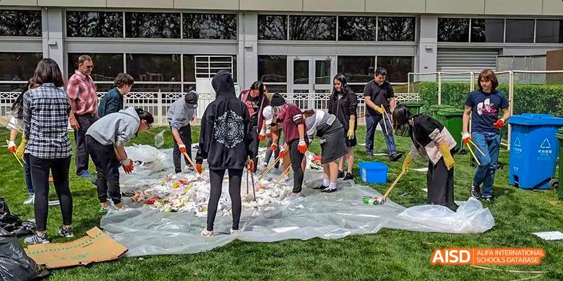 Students from the International School of Beijing work together on a community project, clearing debris from a grassy area.