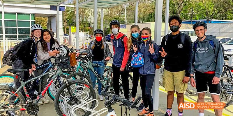 Students and teachers from the International School of Beijing pose for a group photo with their bikes outdoors.