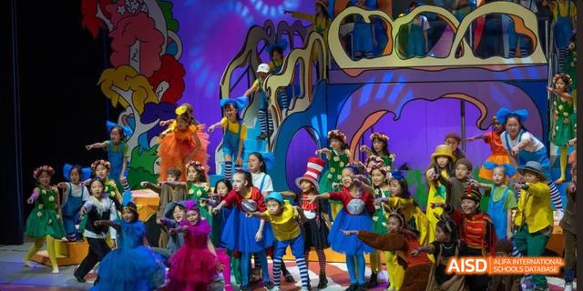 Students from the International School of Beijing are dressed in colorful costumes and posing on a stage with creative backdrops.