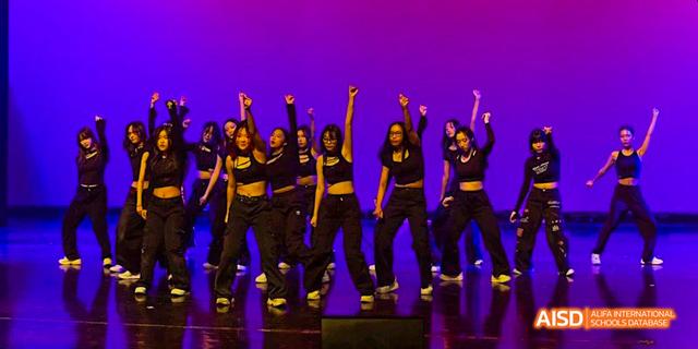 A group of students from the International School of Beijing performs a dance routine on a stage with purple lighting.