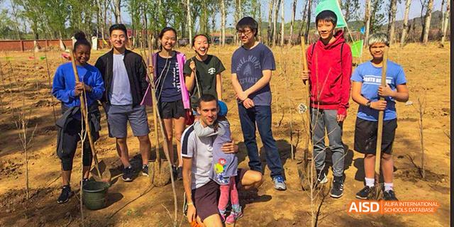 A group of students from the International School of Beijing pose for a picture outdoors in a field.