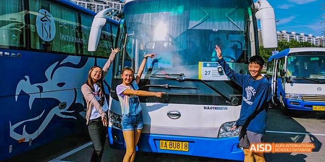 Students from the International School of Beijing pose for a picture in front of a blue school bus.
