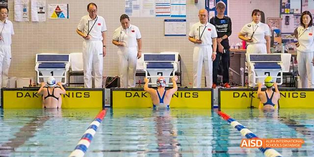 A swim coach and students from the International School of Beijing stand on a platform near the swimming pool.