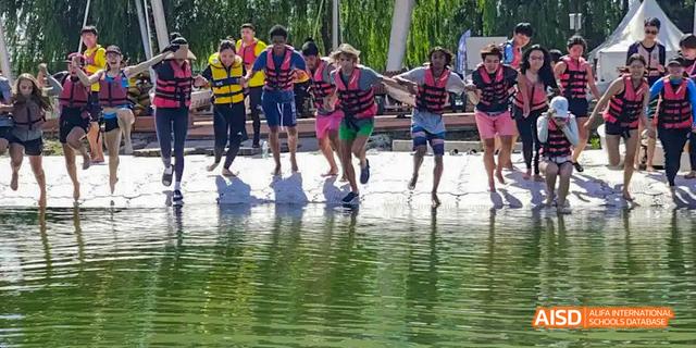 A group of students from the International School of Beijing participate in a fun race, running in a shallow body of water.