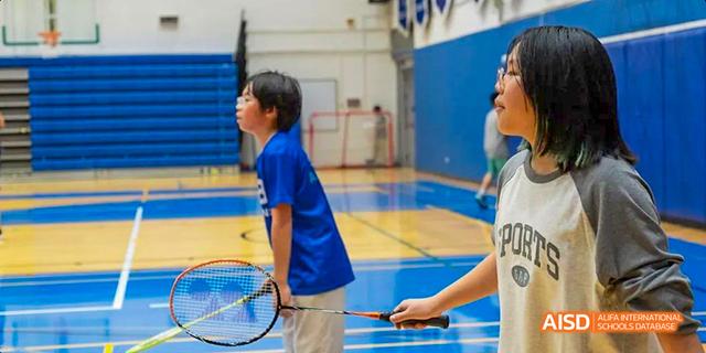 Students from the International School of Beijing play badminton in a gymnasium.