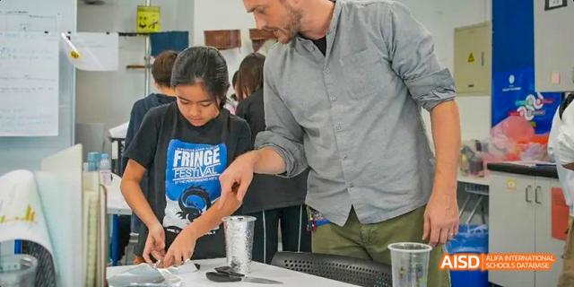 A teacher at the International School of Beijing helps a young student with a science experiment.