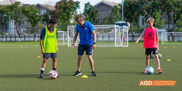 Students from the International School of Beijing play soccer on an outdoor field.