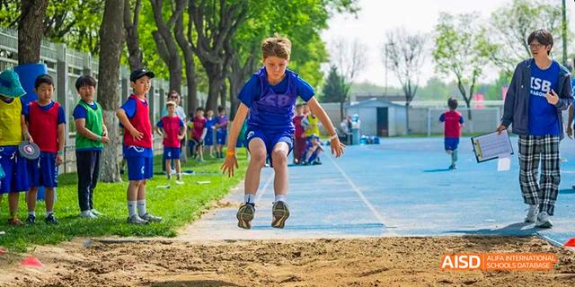 A student from the International School of Beijing runs and jumps during a long jump competition.