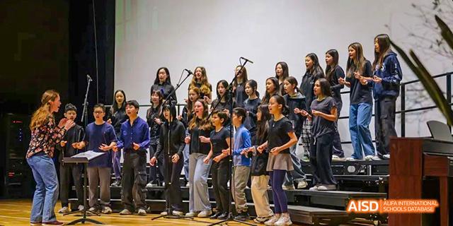 A large group of students from the International School of Beijing pose together for a photo in front of a stage.