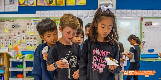 Young students from the International School of Beijing look closely at a device or project.