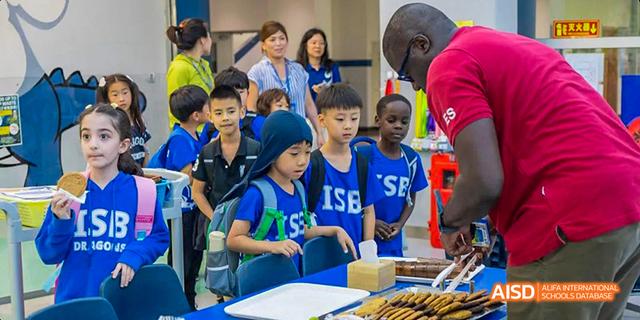Students from the International School of Beijing are shown cooking or preparing food at a table with a teacher.