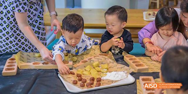A group of young students from the International School of Beijing gather around a large pizza they helped prepare.