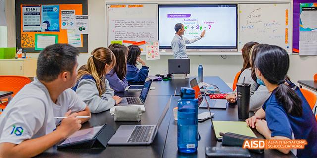International School of Dongguan students sitting at tables with laptops while one student gives a presentation using a large screen in the front of the classroom.