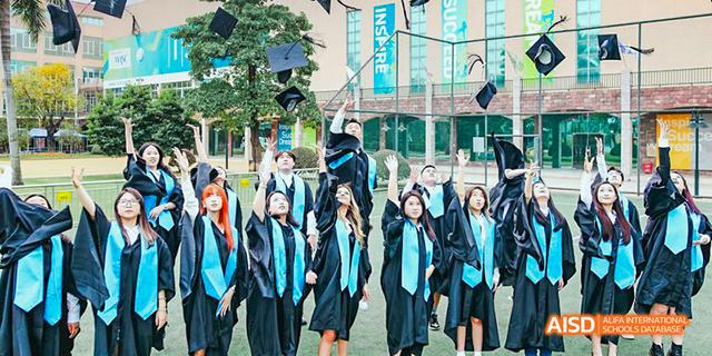 Group of International School of Dongguan students throwing their graduation caps in the air in front of the school building.