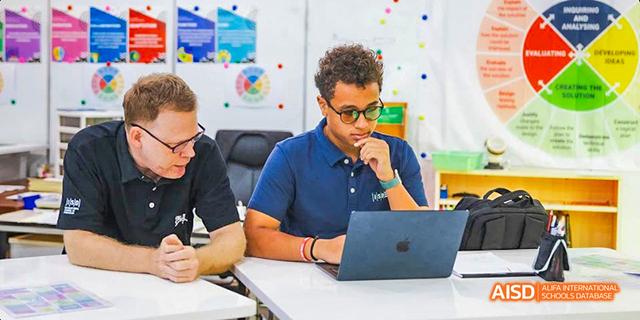 International School of Dongguan student and teacher working collaboratively on a project using a laptop in a classroom setting.