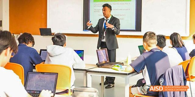 An International School of Dongguan teacher in a suit presenting a lesson to a classroom full of high school students.