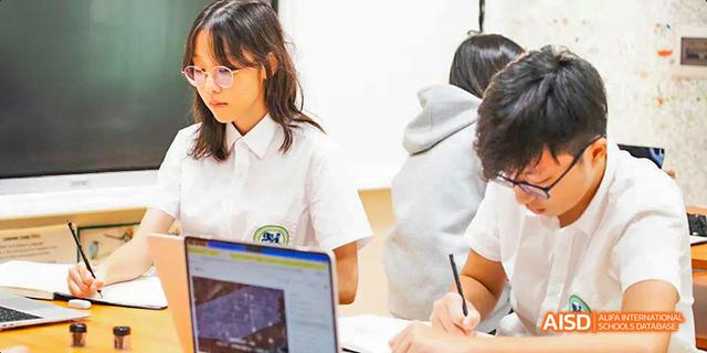 International School of Dongguan student concentrating and writing notes while working on a laptop in a classroom setting.