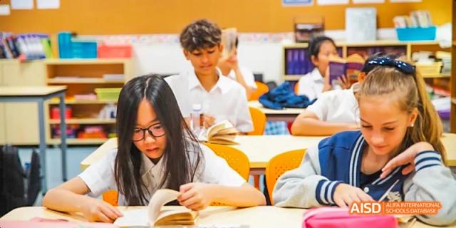 International School of Dongguan student wearing glasses and reading a book at their desk in a classroom.