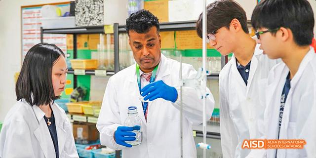 A teacher at International School of Dongguan wearing a lab coat and safety glasses while demonstrating an experiment with students in a science lab.