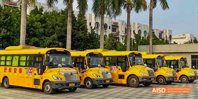 Bright yellow school buses parked outside the main entrance or building of the International School of Dongguan.