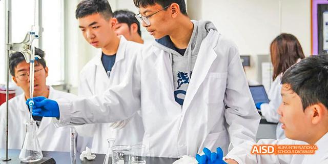 Two International School of Dongguan students wearing lab coats and blue gloves performing a chemistry or science experiment.