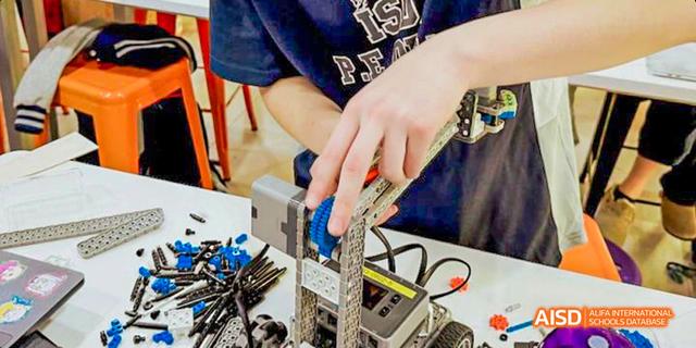 Close-up of an International School of Dongguan student's hands assembling a robot or STEM project using complex building blocks and components.