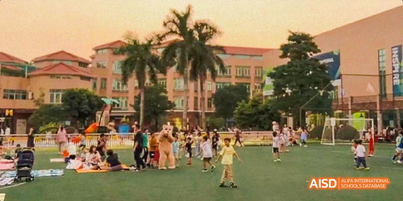 Students and families gather on a grassy field in front of the campus building at International School of Dongguan during an outdoor event.