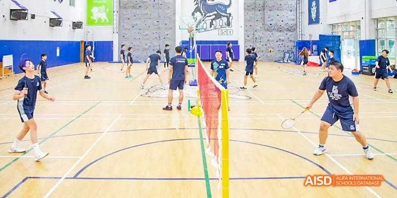 International School of Dongguan students play badminton on an indoor court setup with nets and flags, engaging in a physical education class.