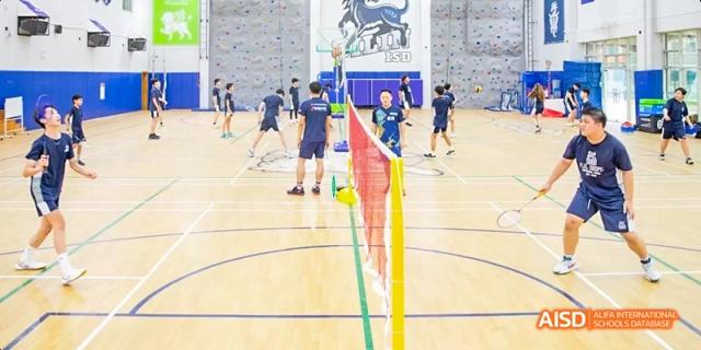 International School of Dongguan students play badminton on an indoor court setup with nets and flags, engaging in a physical education class.