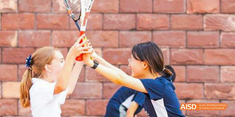 Two International School of Dongguan students high-five with tennis rackets after a match, celebrating a fun and competitive sports victory.