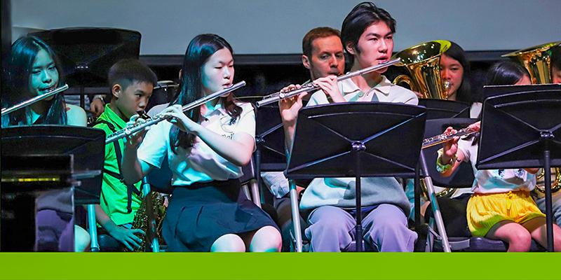 A female student from International School of Dongguan plays the flute, performing music with a fellow band member during a school concert.