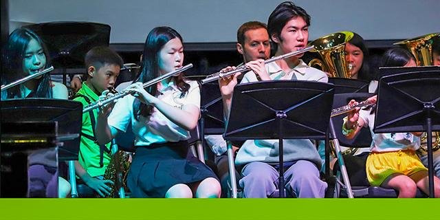 A female student from International School of Dongguan plays the flute, performing music with a fellow band member during a school concert.