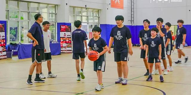 Three young male students from International School of Dongguan walk together on an indoor court, carrying a basketball after practice.