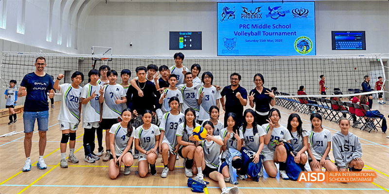 The International School of Dongguan volleyball team, including male and female students and their coach, poses for a group picture indoors.