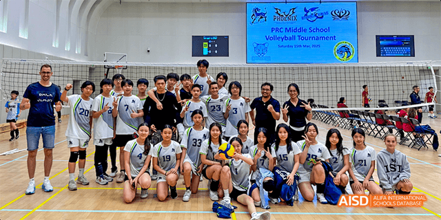 The International School of Dongguan volleyball team, including male and female students and their coach, poses for a group picture indoors.