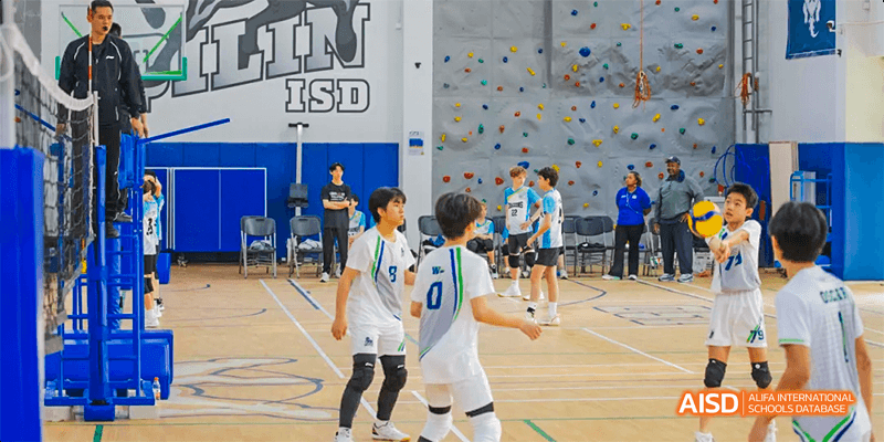 International School of Dongguan students play a competitive indoor volleyball game, focusing on passing and strategy near a school wall.