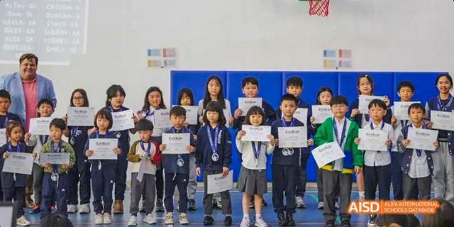 Group of young International School of Dongguan students standing together, holding certificates and wearing medals after an award ceremony or competition.