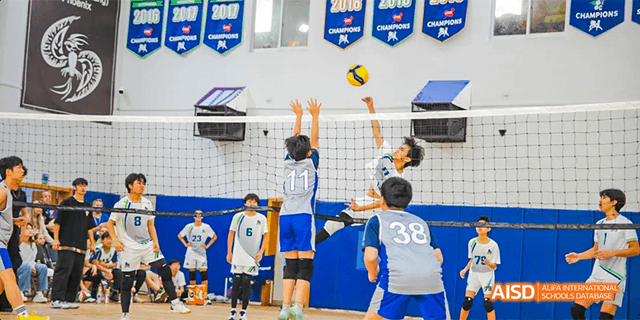 International School of Dongguan students playing volleyball, with one student spiking the ball over the net and others blocking.