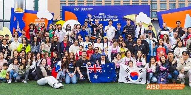 Large, diverse group of students, staff, and families from the International School of Dongguan celebrating Multicultural Day, holding Australian and South Korean flags.