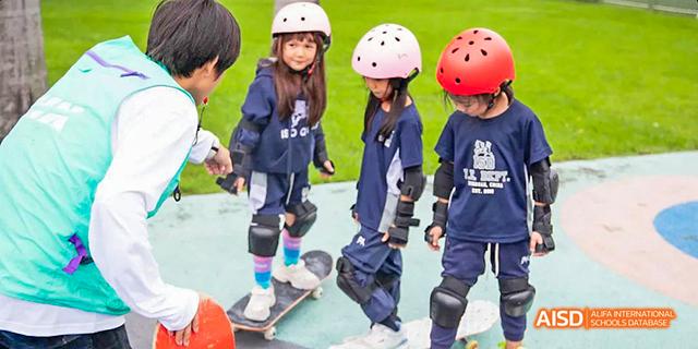 Young students from International School of Dongguan wearing helmets and protective gear while learning to skateboard outdoors.