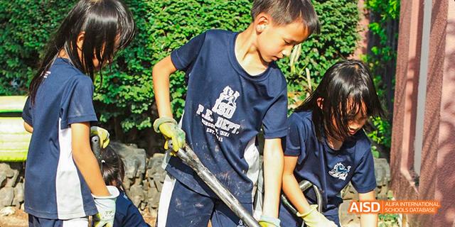 International School of Dongguan students wearing school uniforms and gloves while participating in a community service or environmental project.