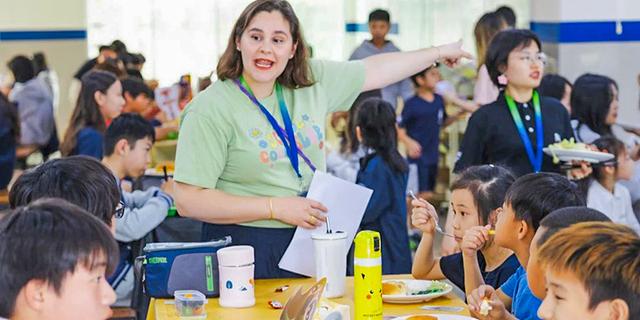 An International School of Dongguan teacher or staff member giving an enthusiastic talk or health lesson to students in a bright setting.