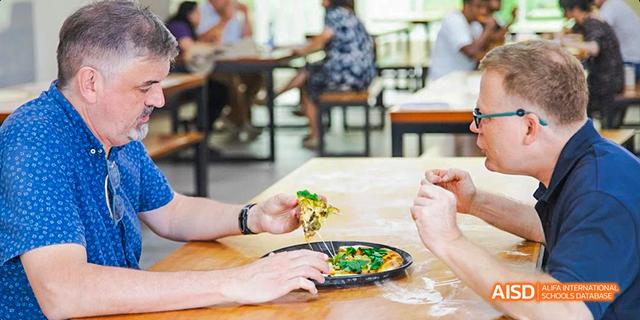 Close-up of two people sharing a healthy, plant-based meal (like a flatbread or pizza with vegetables) at a table at the International School of Dongguan.